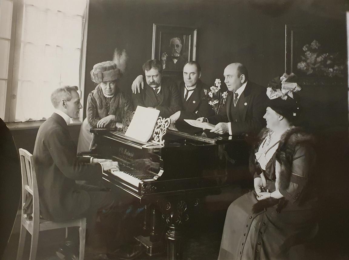 Wilhelm Stenhammar seated at grand piano with musicians and conductors.